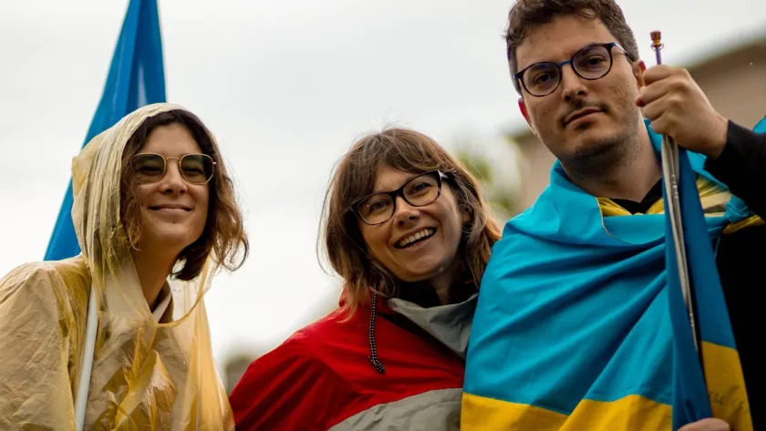 Tre persone avvolte nella bandiera ucraina a una manifestazione a Milano
